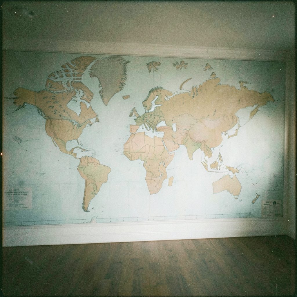 A grainy analog photo of a large world wall map mural covering a room wall, soft sepia and faded teal tones with visible film grain.