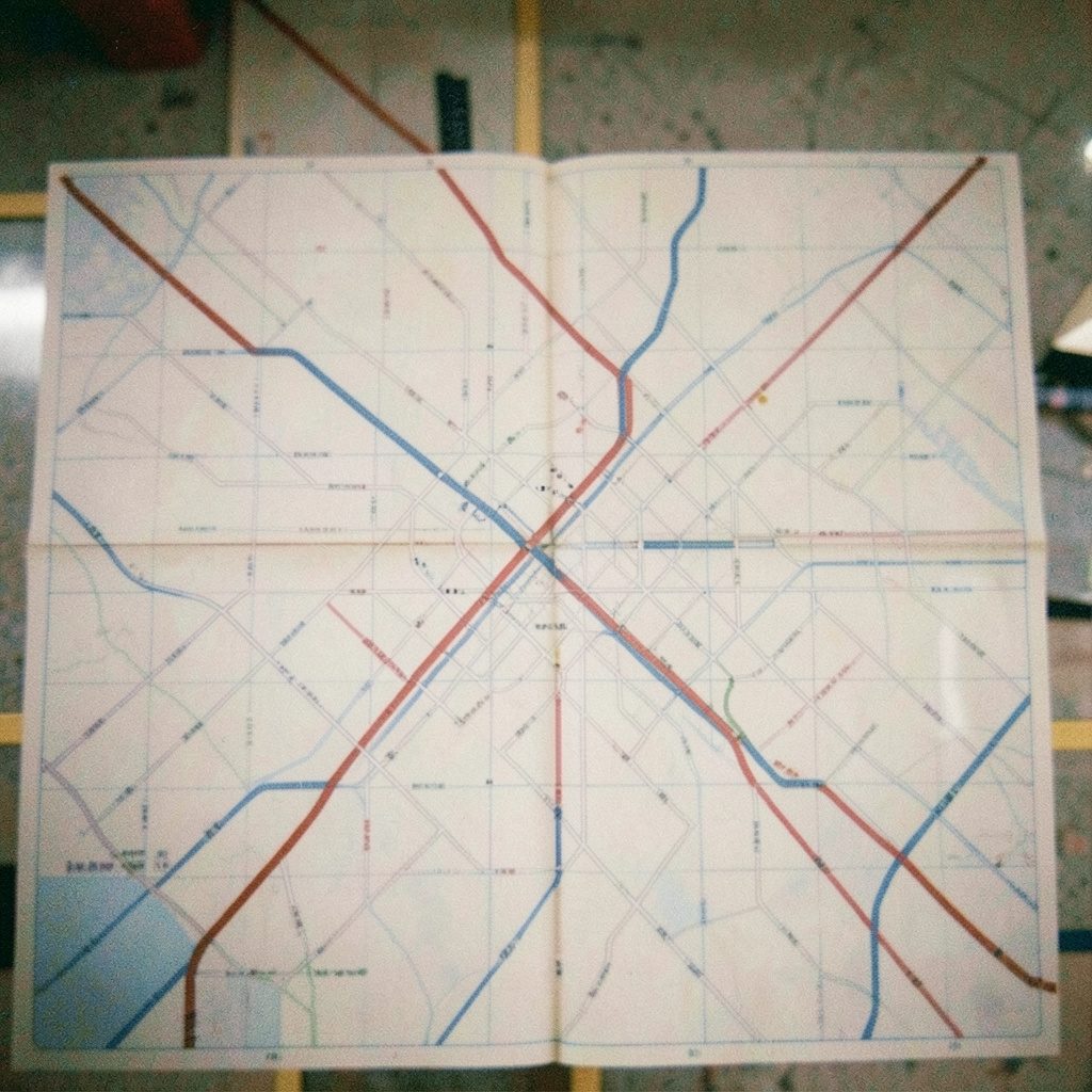 A grainy film photo of a detailed NYC subway map with street grid overlay, soft off-white paper tones with muted blue and red transit lines.